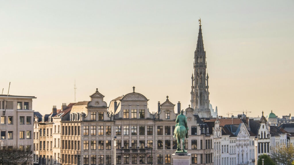 Photo of typical Belgian buildings with a statue in front and the town hall tower in the back