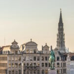 Photo of typical Belgian buildings with a statue in front and the town hall tower in the back