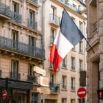 French flag hanging outside a building in Paris, on top of a traffic red light