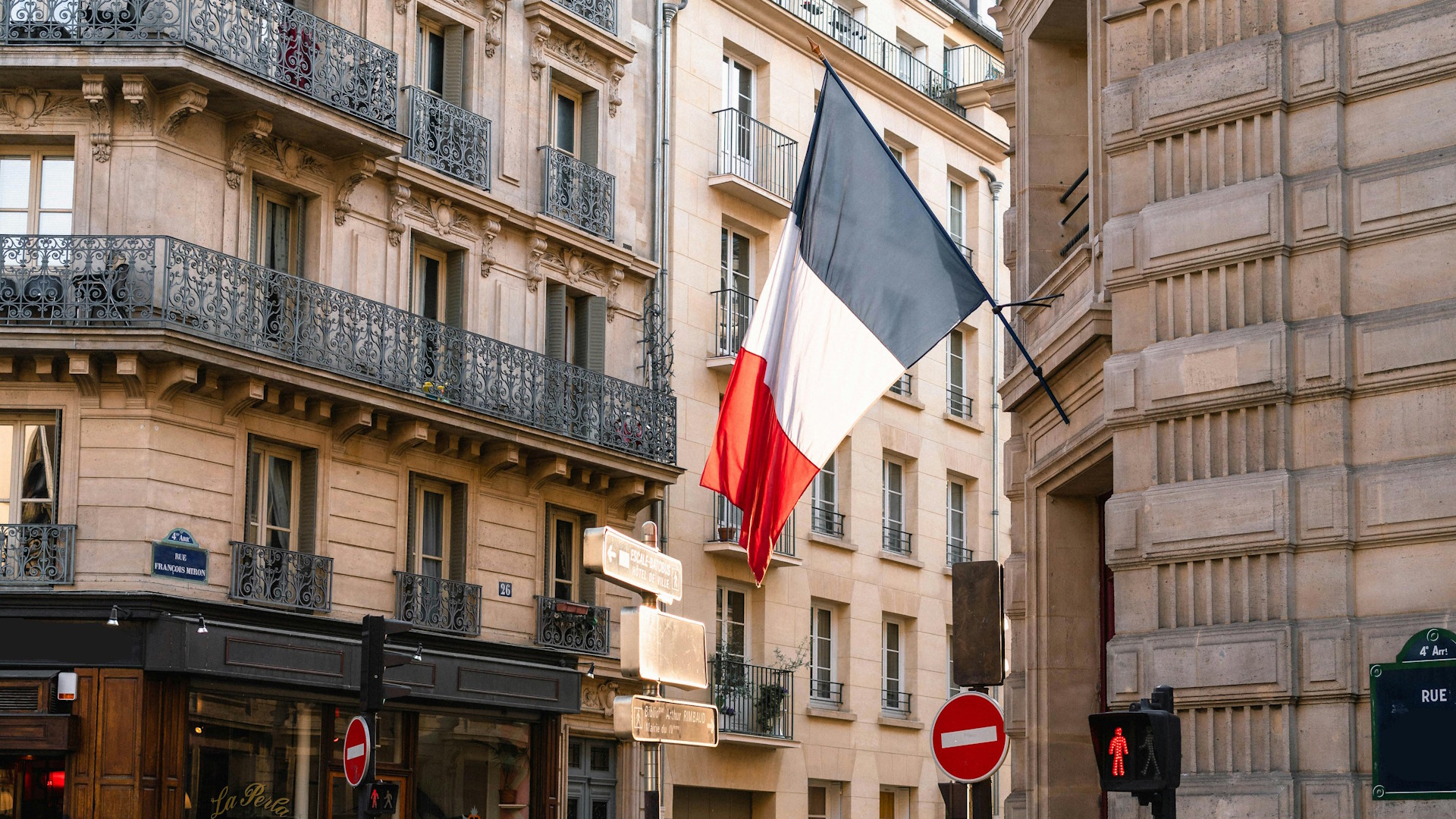 French flag hanging outside a building in Paris, on top of a traffic red light